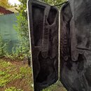 Otevřený tvrdý kufr na hudební nástroj s černým plyšovým vnitřkem. Vnitřek je tvarován pro umístění kytary. Kufr má stříbrný kovový rám a černou ruko…