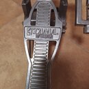Detailní pohled na kovový pedál basového bubnu stříbrné barvy. Na horní části je vyryto logo TAMA a pod ním název modelu IMPERIAL STAR. Povrch pedálu…