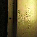 Detail zlatavého kovového povrchu s vyrytými nápisy. Je zde uveden text „scoutronics“, „CARY, IL“, „PAT 2,982,819“, „3,106,610“ a „MADE IN U.S.A.“. V…