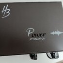 Černý kovový box s nápisem Power ATTENUATOR a grafickým symbolem zvukové vlny. V levém horním rohu je bílé logo znázornující stylizované písmeno H s…