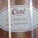 Oválná štítková nálepka vnitřku kytary s červeným okrajem. Je na ní uveden nápis Cort GUITARS, MODEL: CJ-MEDX NAT a SERIAL NO: IA250786331. Dole je u…