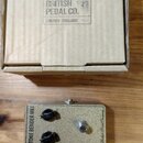Kartonová krabice s nápisem BRITISH PEDAL CO. LONDON - ENGLAND. Pod ní je efekt pedál v béžovém provedení s kovovým spínacím tlačítkem a dvěma černým…