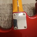 Detail spoje krku a těla červené elektrické kytary. Na dřevěném krku je nápis MADE IN JAPAN. Spojení je zakryto kovovou čtvercovou deskou připevněnou…