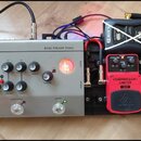 Sestava efektů na černém pedalboardu. Vlevo je stříbrný pedál s nápisy MODULE, TERRA-NOVA a BASS PREAMP PEDAL. Uprostřed je červený pedál s nápisy CO…