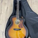 Akustická kytara s vyvedeným korpusem v provedení sunburst, položená v černém měkkém pouzdře. Na hlavě nástroje je bílý nápis GUILD. Kytara má hnědý…