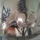 Stříbrný, lesklý činel s viditelným broušením. Na povrchu jsou černé nápisy Zildjian, Custom a CRASH. Povrch je v dobrém stavu s výrazným odleskem.