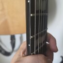 Detailní pohled na hmatník a hranu krku elektrické kytary s černým povrchem. Na hraně krku jsou vidět bílé značky (inlaye). Struny jsou upevněny pomo…