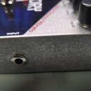 Detail kytarového efektu v kovovém šasi s broušeným povrchem. Na horní straně je modré pole s bílými nápisy „Electro-Harmonix“, „INPUT“ a „Israel/Dio…