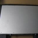 Stříbrný obdélníkový elektronický přístroj v kartonové krabici s pěnovou výplní. Fotografie zachycuje horní plochu přístroje, která je hladká a připe…