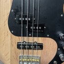 Detail těla elektrické basy z přírodního dřeva s černým pickguardem. Na nástroji jsou tři snímače, z nichž dva mají bílý nápis Seymour Duncan. Kovový…