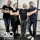 Fotografie zobrazuje čtyři osoby stojící vedle sebe před perforovaným akustickým panelem. V levém dolním rohu je bílý nápis HEBLO VE ČTYRECH. Muž vle…