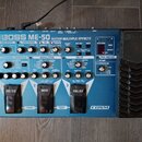 Modrý efektový pedál Boss ME-50 Guitar Multiple Effects. Na horní straně jsou různé ovládací knofíky, přepínače a červené digitální displeje. V dolní…