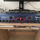 Modrý kytarový procesor s kovovým šasi a názvem V-AMP PRO a logem BEHRINGER. Na předním panelu jsou ovládací knofíky, červené tlačítka A až E a digit…