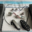 Sada elektroniky pro elektrickou kytaru rozmístěná na bílém podkladu. Soubor obsahuje dva chromované knofíky, jeden přepínač, potenciometr, vstupní j…