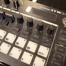 Černý elektronický nástroj s nápisem GROOVEBOX mc-101. Zařízení obsahuje bílé klávesy s označením tónů, několik černých otočných potenciometrů a řadu…