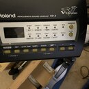 Černý elektronický perkusní modul Roland s bílým panelem ovládání. Na spodní části je nápis PERCUSSION SOUND MODULE TD-3 a logo V-Drums. Modul obsahu…