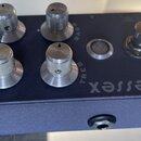 Modrý kytarový efekt s kovovým šasi. Na horní straně jsou čtyři stříbrné knoflíky s nápisy LEVEL, GAIN, BASS a TREB, jeden stříbrný přepínač a jedno…