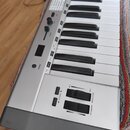 Stříbrný klávesový nástroj s černými a bílými klávesami. Na ovládacím panelu jsou nápisy POWER, VOLUME, DIGITAL, ALL NOTES, CHORD, OCTAVE a MODULATIO…