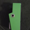 Detailní pohled na boční stranu zeleného hudebního přístroje nebo příslušenství. V horní části je vidět kovový konektor (jack). Povrch je hladký, bez…