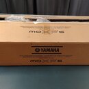 Hnědý cardboardový přepravní karton s nápisy. Na krabici je dvakrát uveden text MUSIC PRODUCTION SYNTHESIZER / SYNTHÉTISEUR DE PRODUCTION MUSICALE SI…