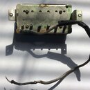 Kovový elektrický komponent s montážními úchyty po stranách. Povrch vykazuje známky koroze, oxidace a opotřebení. Z komponentu vychází kabel v kovové…