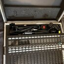 Černý digitální mixážní pult s bílými popisky a posuvníky, na kterém je uveden nápis MIDIPLUS a FIT. Zařízení je umístěno v otevřeném hliníkovém kufr…