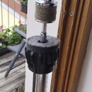 Detail horní části chromovaného stojanu s černým plastovým utahovacím knoflíkem. V horní části je umístěn držák s šroubovací spojkou a hnědým tlumicí…