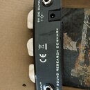 Fotografie zachycuje zadní stranu černého efekt pedálu s třemi bílými knoflíky. Na povrchu jsou nápisy 9V DC OUTPUT, INPUT a EAST SOUND RESEARCH DENM…