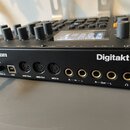 Černý sampler Digitakt II značky Elektron. Na zadním panelu jsou vidět konektory pro napájení s nápisem 12VDC 1A, USB, MIDI Thru, MIDI Out, MIDI In a…