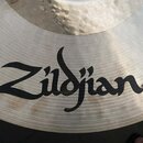 Detailní záběr na povrch kovového činele stříbrné barvy s viditelným broušením. Na povrchu je umístěno černé logo Zildjian s registraceční značkou ®.…