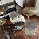 Bílá bicí souprava s chromovaným kováním, která obsahuje basový rám, dva tom-tomy a tři činely. Na činelech je vidět logo Byzance a nápis MEINL, na b…