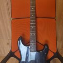 Černá elektrická kytara s tmelem v barvě přírodního dřeva. Na hlavě je viditelné logo Squier. Kytara má tři snímače, chromovaný most a ovládací knofl…
