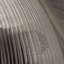 Detailní záběr na povrch kovového činely s koncentrickými drážkami. Na povrchu je vyražen nápis MEINL, MADE IN GERMANY, ROLAND MEINL a číslo 41013296…