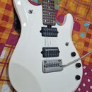 Bílá elektrická kytara s hnědým hmatníkem a dvěma černými humbuckery. Nástroj je vybaven chromovaným tremolo mostem s páčkou a třemi černými ovládací…