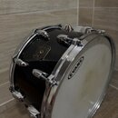 Černý buben s chromovaným obručováním a ladidly. Na koruse je viditelný zlatý štítek s nápisem GRETSCH USA CUSTOM. Na bláně je umístěno logo EVANS, s…