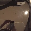 Fotografie zachycuje černý, lesklý plech s odrazivým povrchem, pravděpodobně pickguard do elektrické kytary. V horní části je umístěna malá černá pla…