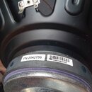Detail zadní části černého reproduktoru s kovovým magnetem. Na černém rámu jsou dvě nálepky s nápisy PN:2042756 a 086018B60955. V horní části je vidě…