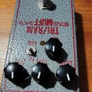 Kytarový efekt v šedém texturovaném provedení s červeným rámečkem. Na horní straně je nápis TRI/RAM MUFF a v horním okraji nápis BASIC AUDIO. Pedal m…