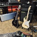 Fotografie zachicuje studiový koutek s dvěma elektrickými kytarami na stojáncích. Vlevo je černá polodupatá kytara a vpravo krémová kytara typu Strat…