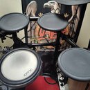 Elektronická bicí souprava s černými pady a černým rámem. Na třech padách je viditelné logo YAMAHA a na největším padu nápis DTX drums. Povrchy padů…