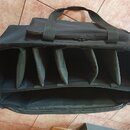 Černý textilní přepravní kufr s rukojetí. Vnitřní prostor je rozdělen na pět oddělených přihrádek. Na povrchu nejsou viditelné žádné značky ani nápis…