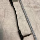 Černý audio kabel s konektory typu jack na obou koncích. Kabel je položen vedle stahovacího metru, který ukazuje délku přibližně 20 cm. Na plastovém…