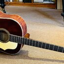 Akustická kytara s tmavě hnědým, lakovaným povrchem těla a viditnou masivní strukturou dřeva na bocích. Nástroj má světlý pickguard a tmavý hmatník s…