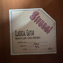 Fotografie detailu štítku uvnitř akustické kytary. Na štítku je fialové logo Shunda a nápisy CLASSICAL GUITAR, MADE IN LUBY, CZECH REPUBLIC. Ručně do…