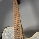 Elektrická kytara s krčkem z jasného dřeva a bílým tělem. Kytara má bílý pickguard s mramorovaným vzorem a jeden viditelný snímač v chromovém rámečku…