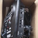 Černý elektronický modul v kartonové krabici, obklopený černými kabely. Na zadní straně jsou viditelné konektory s popisky: DC IN, PHONES, L/MONO OUT…
