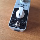 Kytarový efekt v šedém kovovém šasi s černým ovládacím panelem. Na horní části je nápis e-lady a v dolní části jsou popisky INPUT, OUTPUT, RANGE, COL…