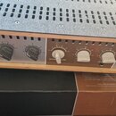 Stříbrný audio zesilovač s dřevěným šasi. Na předním panelu je nápis UNIVERSAL AUDIO a logo, tři černé a tři bílé otočné ovířkovací knoflíky s popisk…