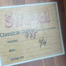 Fotografie detailu štítku klasické kytary přilepeného na dřevěný povrch. Štítek nese velký růžový nápis Strunal a text Classical Guitar Made in Luby,…