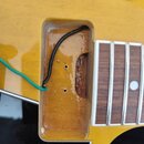 Detailní pohled na vyfrézovaný prostor v žlutém těle elektrické kytary. Uvnitř jsou vidět dva černé vodiče, jeden z nich je zelený a vede mimo výřez.…